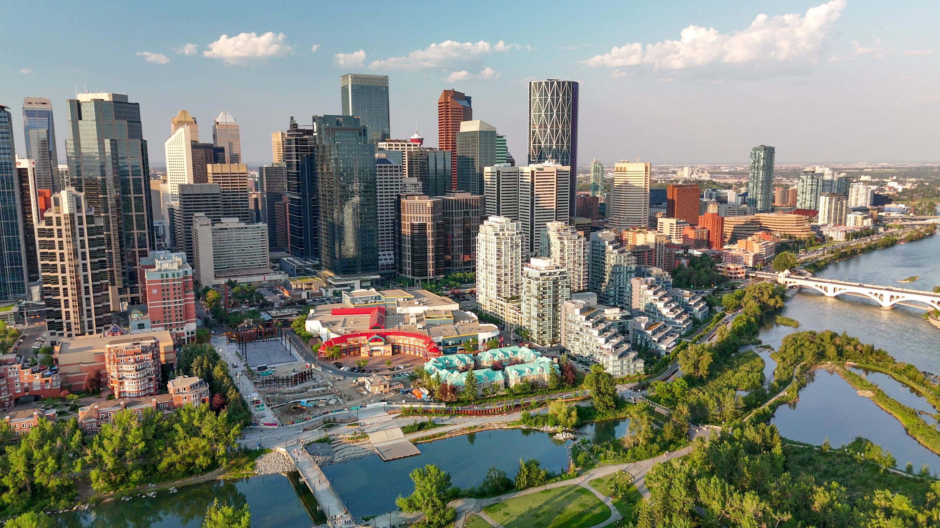 A vibrant cityscape with modern buildings and a park area under a blue sky.